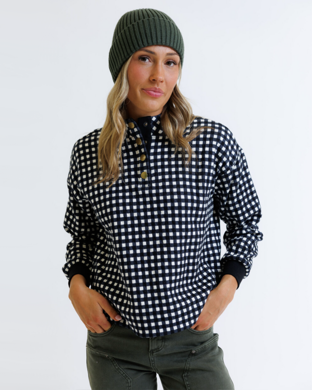 Woman wearing a black and white checkered shirt with a green beanie on a light gray background