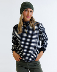 Woman wearing a black and white checkered shirt with a green beanie on a light gray background