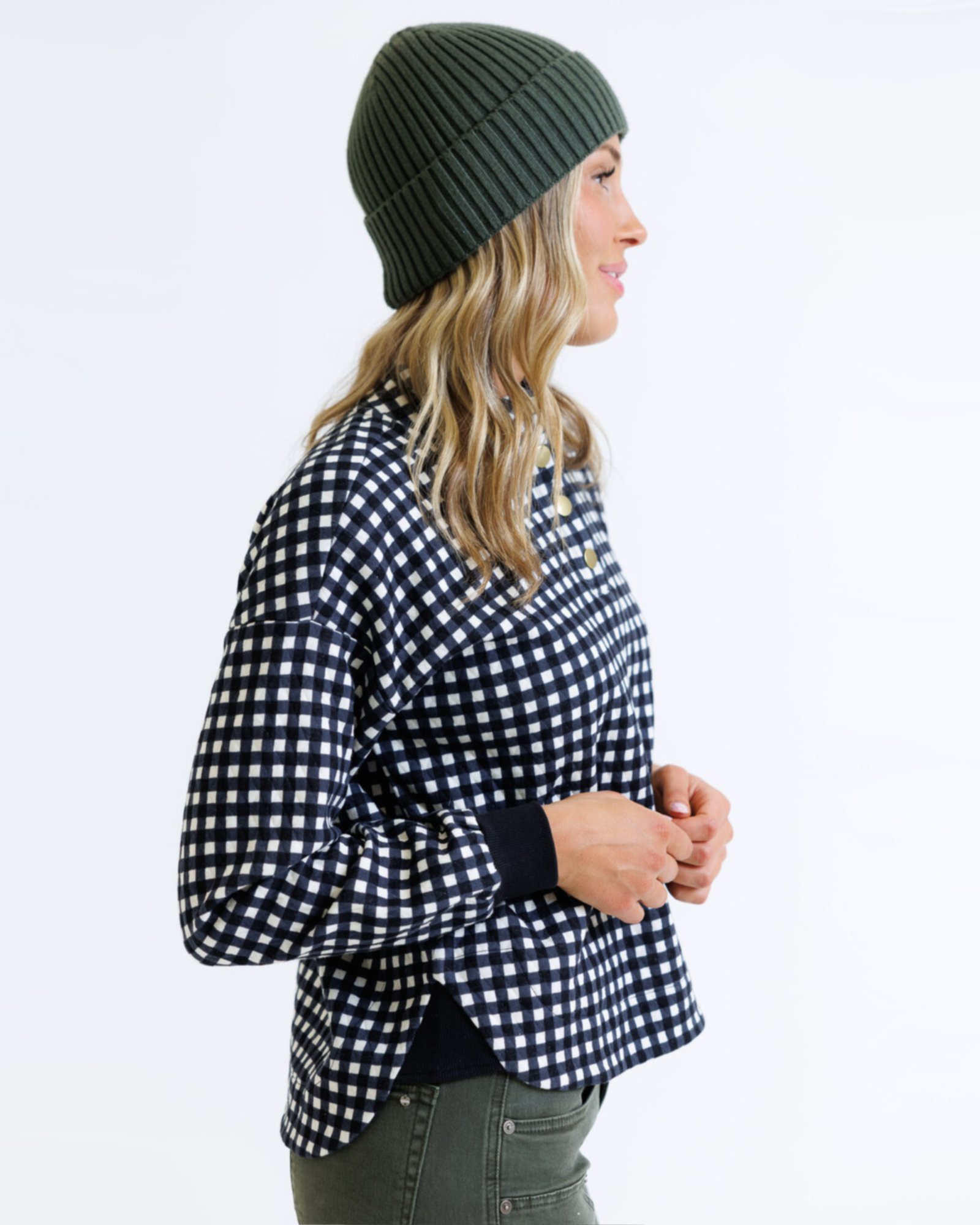 Woman wearing a black and white checkered shirt with a green beanie on a white background