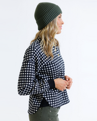 Woman wearing a black and white checkered shirt with a green beanie on a white background