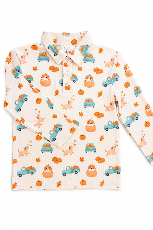 A long-sleeve collared children's shirt in a warm cream color, featuring an all-over autumn-themed print of orange pumpkins, teal pickup trucks, and light brown dogs with orange leaves.