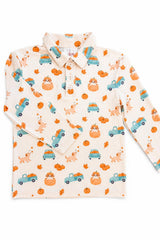 A long-sleeve collared children's shirt in a warm cream color, featuring an all-over autumn-themed print of orange pumpkins, teal pickup trucks, and light brown dogs with orange leaves.