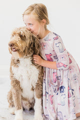 Young girl in a patterned dress hugging a large brown and white dog on a light background