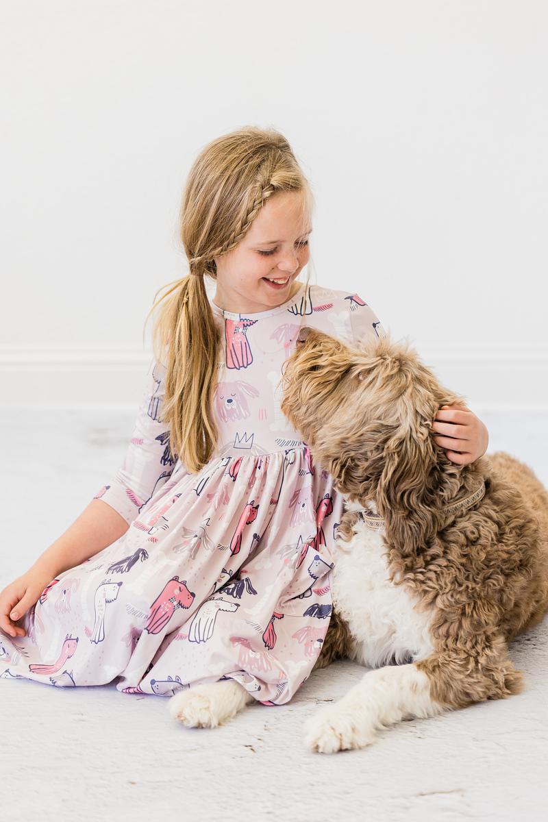 Young girl in a patterned dress sitting on the floor with a dog.