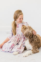 Young girl in a patterned dress sitting on the floor with a dog.
