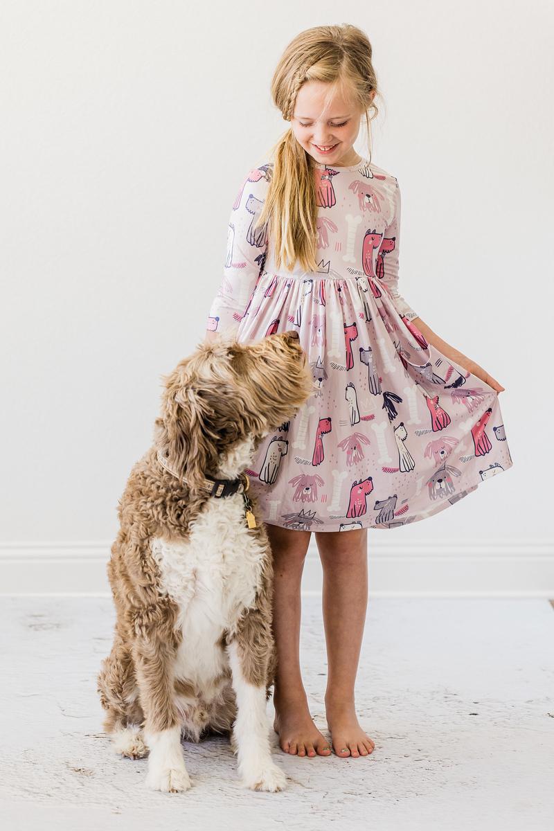 Young girl in a patterned dress standing next to a dog on a white floor.