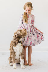 Young girl in a patterned dress standing next to a dog on a white floor.