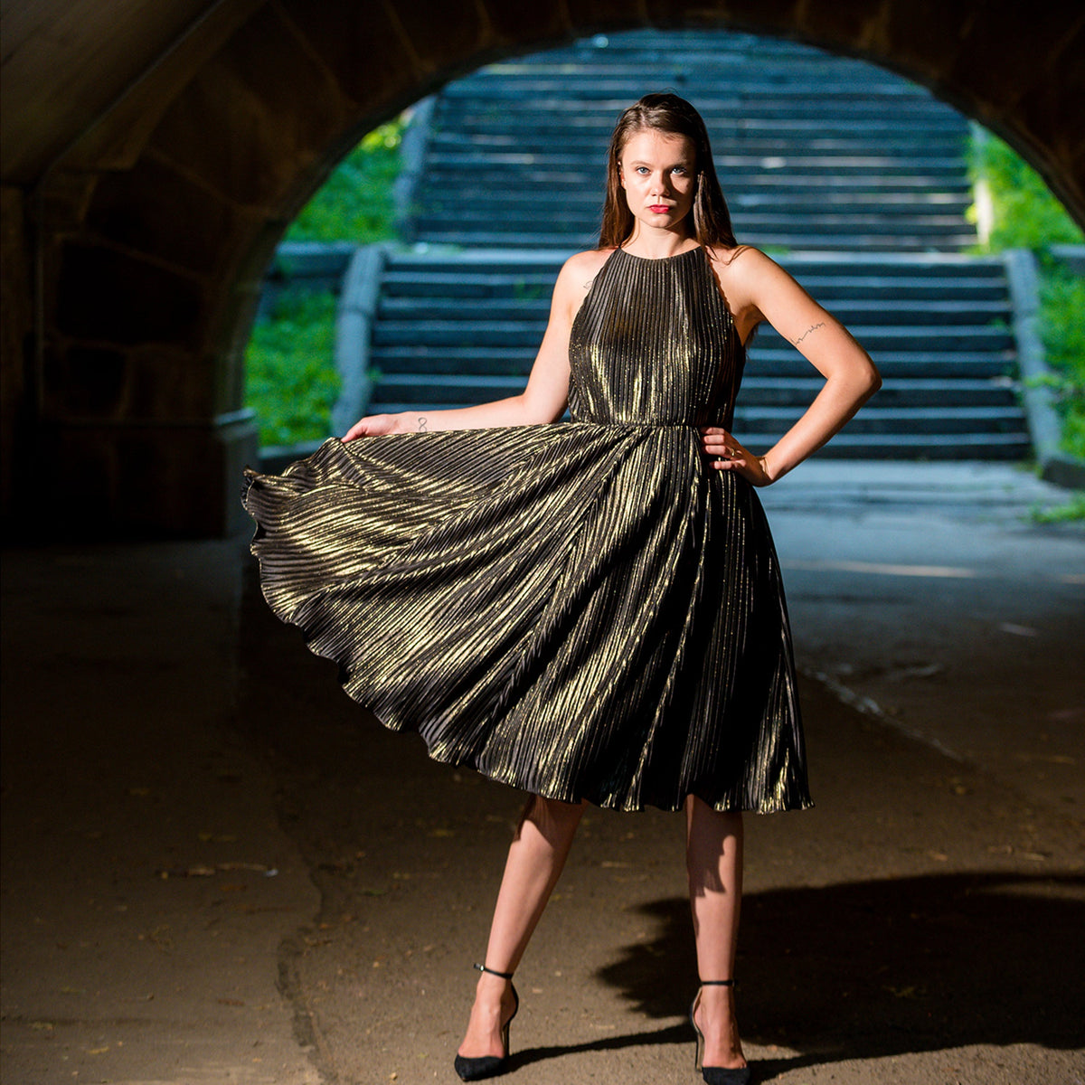 Woman in a gold metallic dress standing under an archway with greenery in the background
