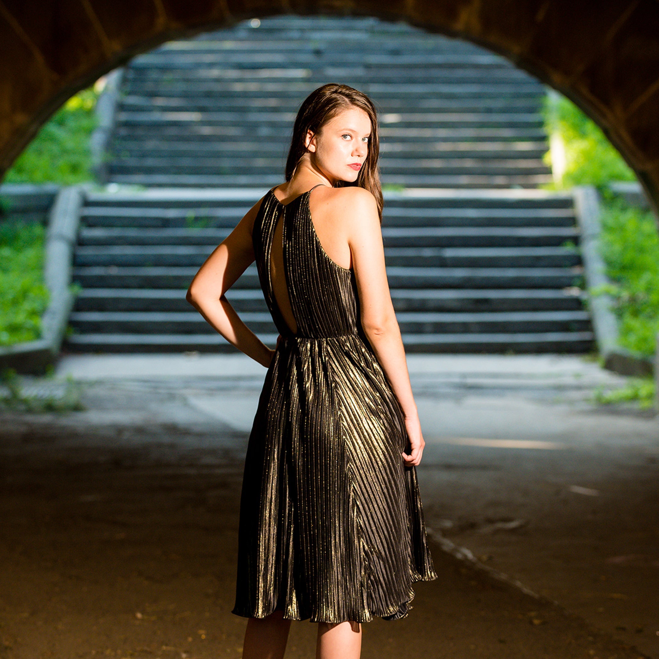 Woman in a gold dress standing under an archway with steps in the background