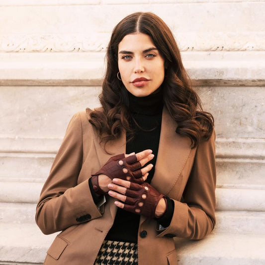 Woman wearing a brown coat and gloves against a light-colored wall.