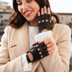 Woman wearing a beige coat and black fingerless gloves outdoors.