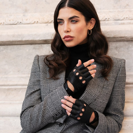 Woman wearing black leather gloves and a gray checkered coat against a stone wall.