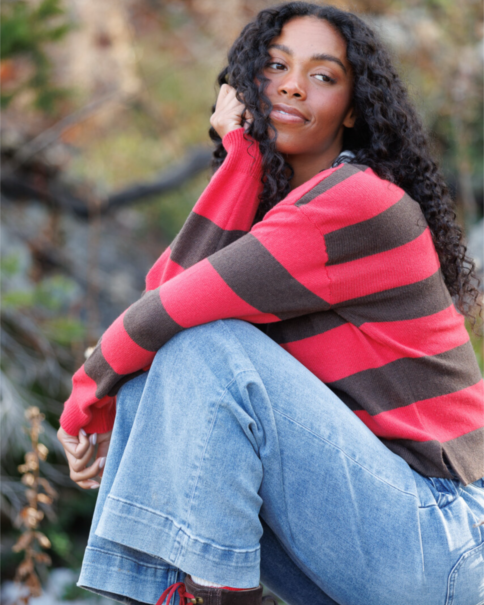 Woman wearing a red and brown striped sweater sitting outdoors.