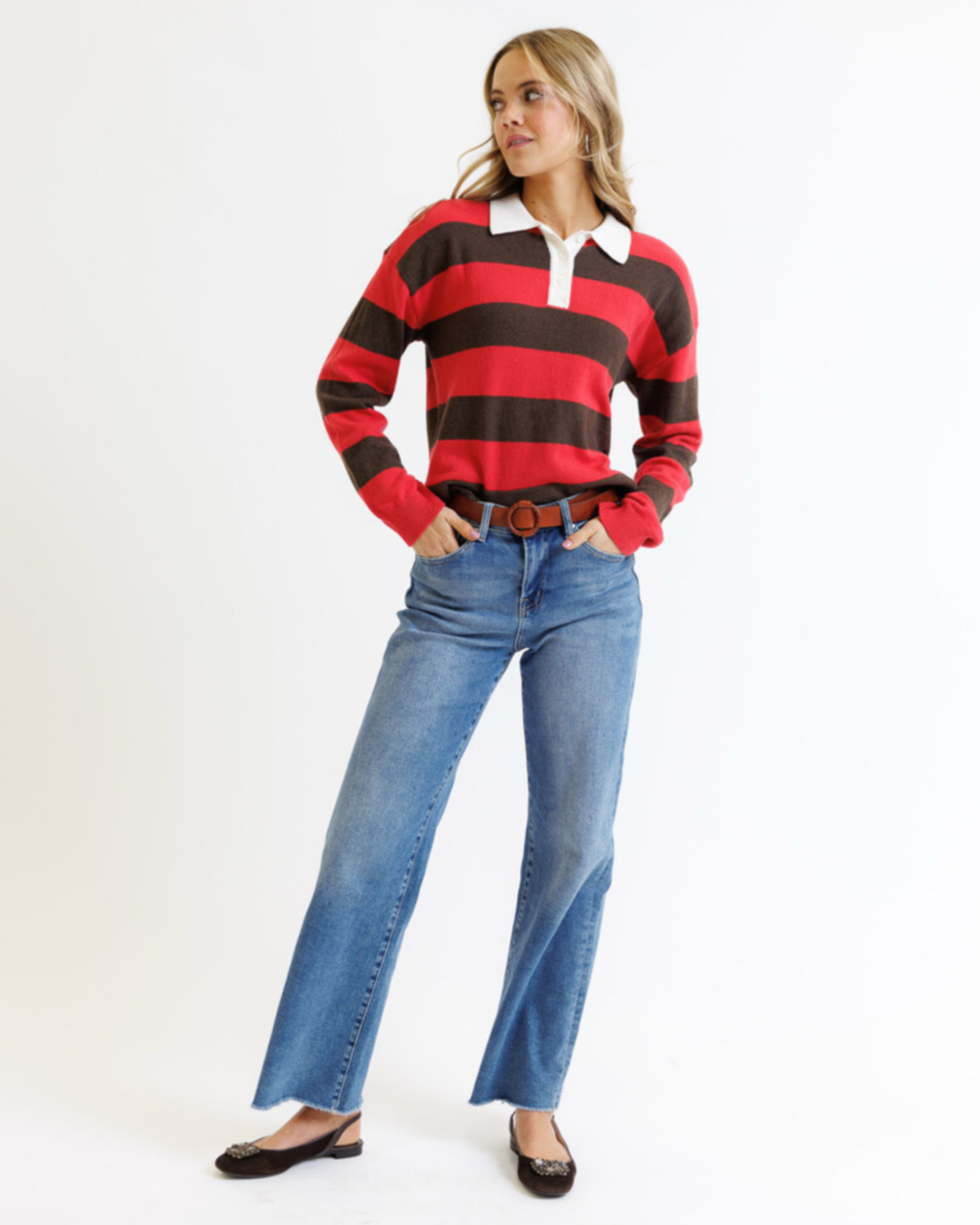 Woman wearing a red and brown striped sweater with a white shirt underneath, paired with blue jeans on a white background.