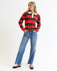 Woman wearing a red and brown striped sweater with a white shirt underneath, paired with blue jeans on a white background.