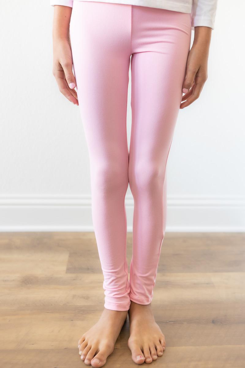 Person wearing pink leggings on a wooden floor with a white wall background