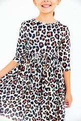 A child wearing a white three-quarter sleeve dress with a black and dusty rose leopard print, shown against a plain white background.