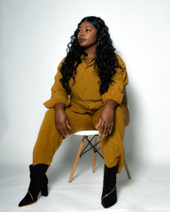 Woman in mustard yellow outfit sitting on a white chair against a white background