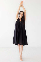 Woman wearing a black dress standing with arms raised against a white background