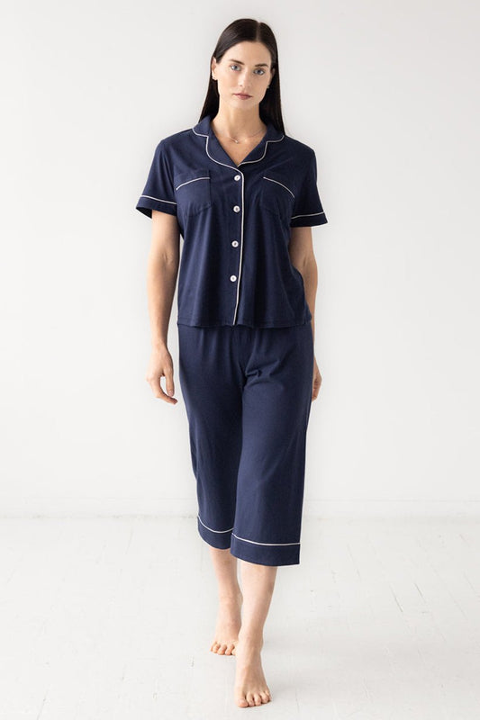 Woman wearing navy blue pajama set with white trim on a white background