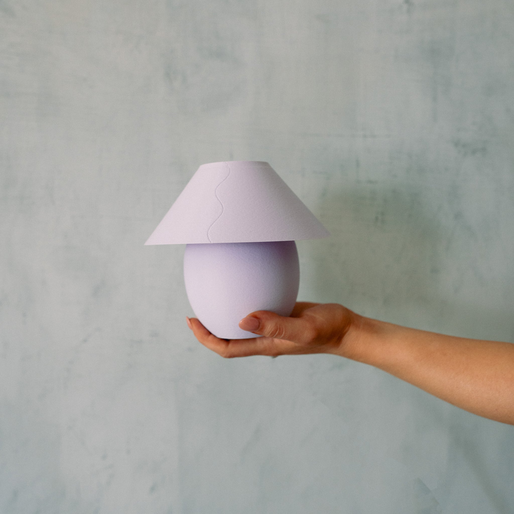 Hand holding a small purple lamp against a gray background