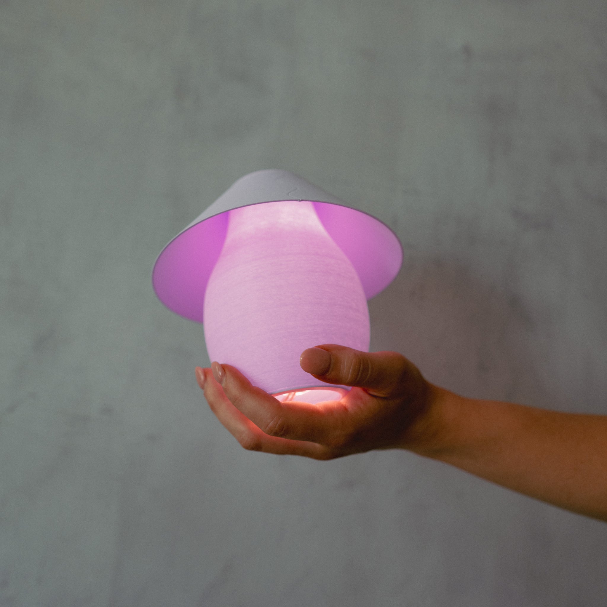 Hand holding a pink mushroom-shaped lamp against a gray background