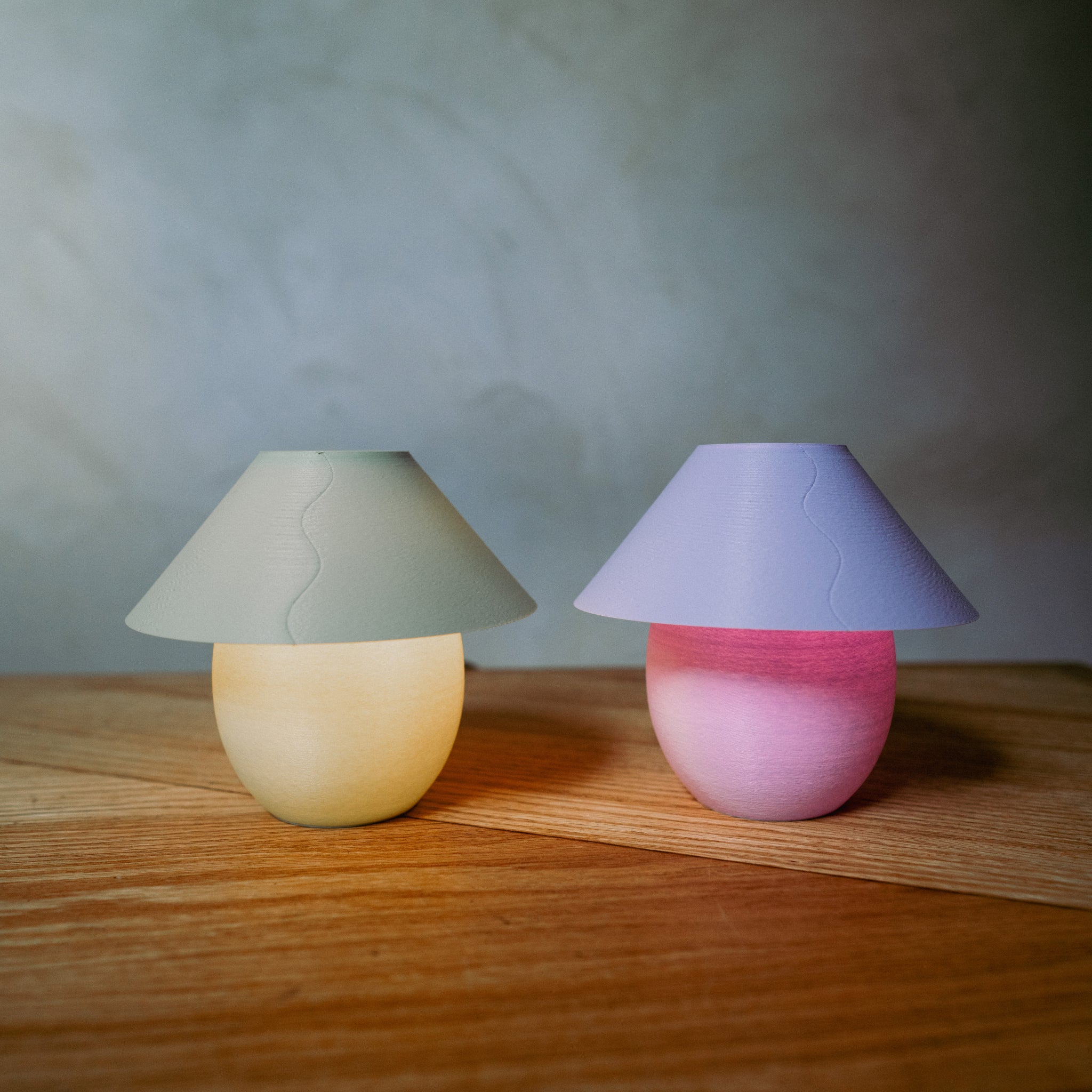 Two colorful mushroom-shaped lamps on a wooden surface with a neutral background
