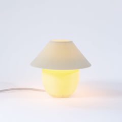 Small lamp with a beige shade and yellow base on a light gray background