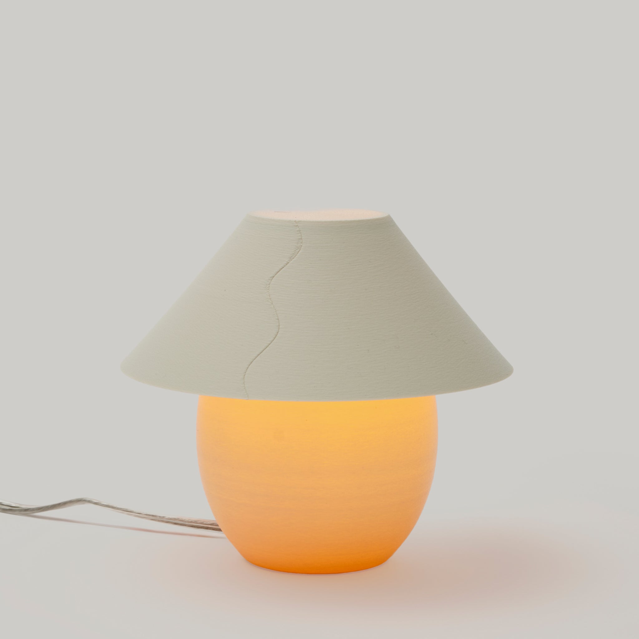 Table lamp with a beige shade and orange base on a light gray background