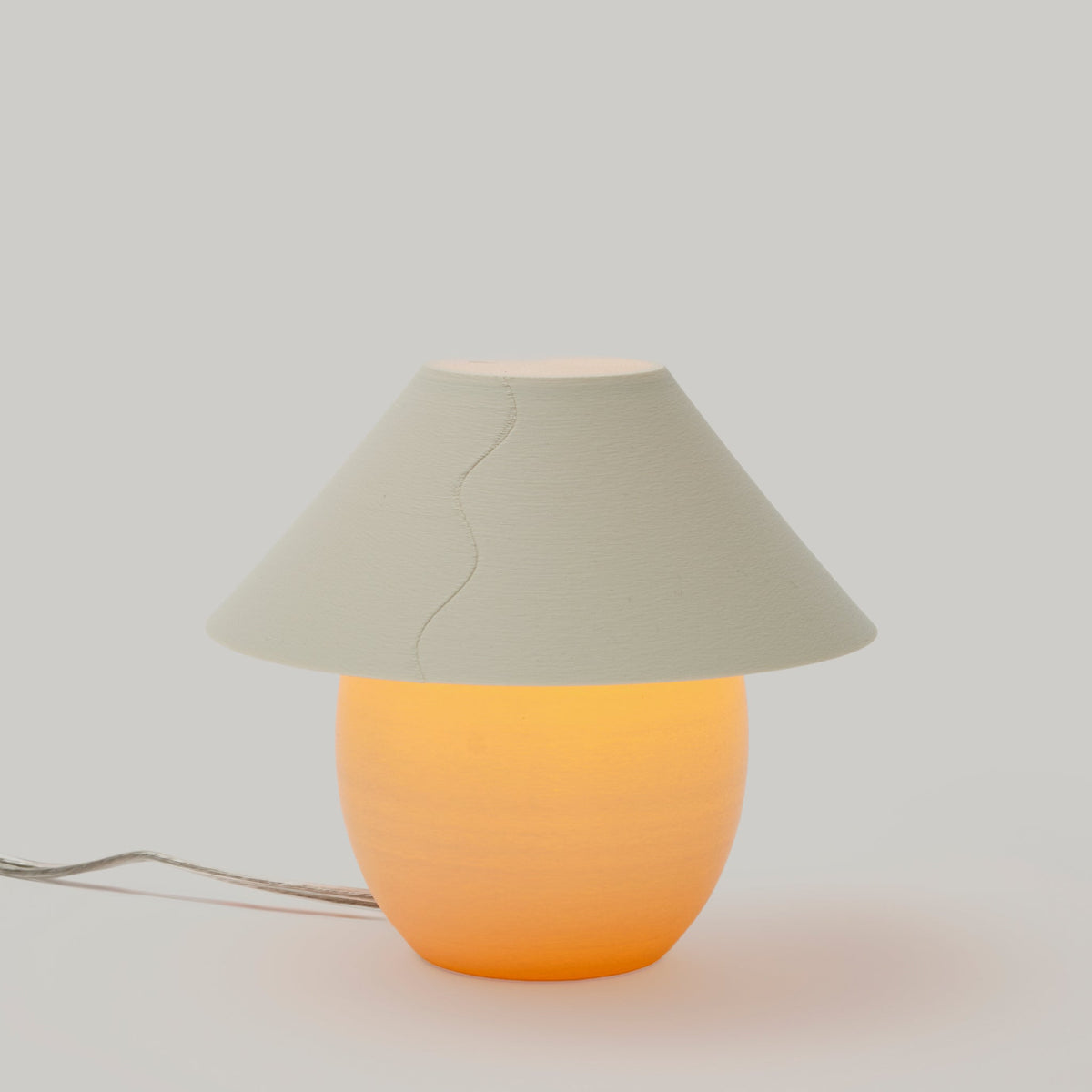 Table lamp with a beige shade and orange base on a light gray background