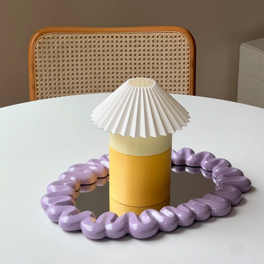 Decorative lamp with a white shade and purple base on a table.