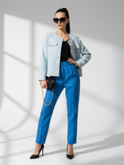 Woman wearing a light blue jacket, black top, and blue pants on a white background