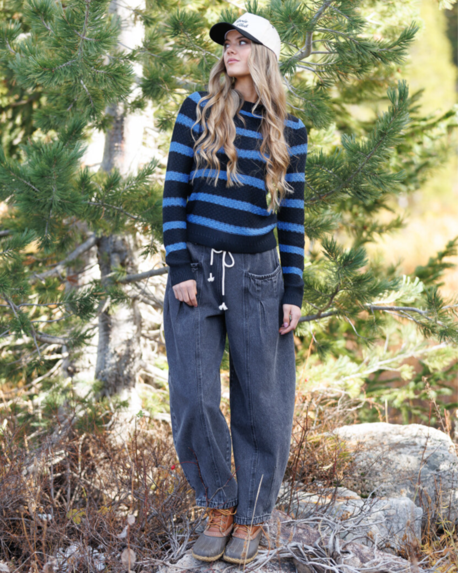 Woman wearing a striped sweater and jeans standing in a forest setting