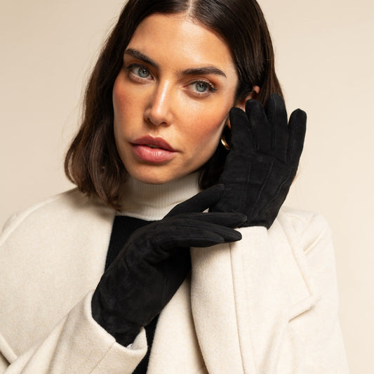 Woman wearing black gloves and a white coat against a beige background