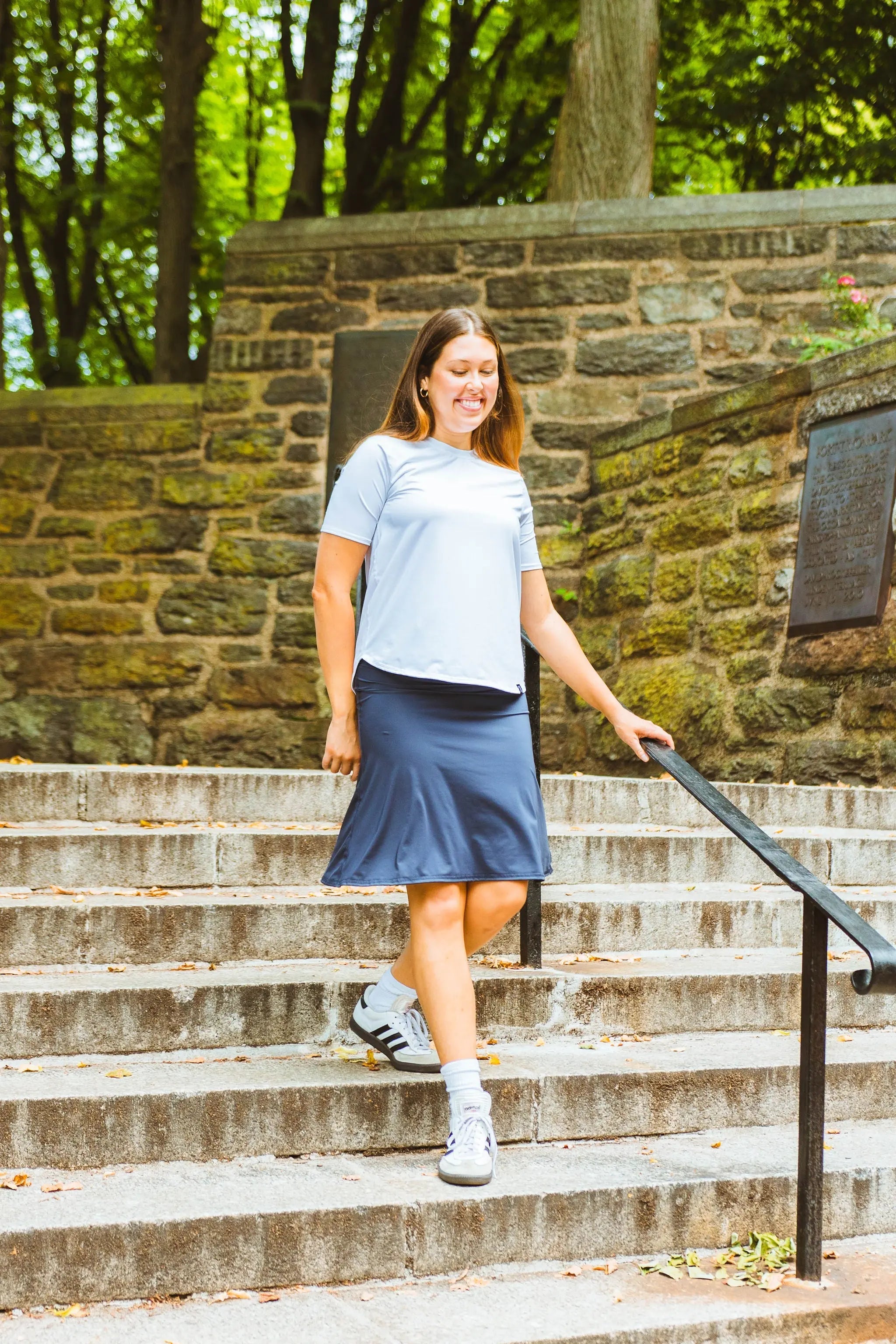 Woman walking up stone steps outdoors with greenery in the background
