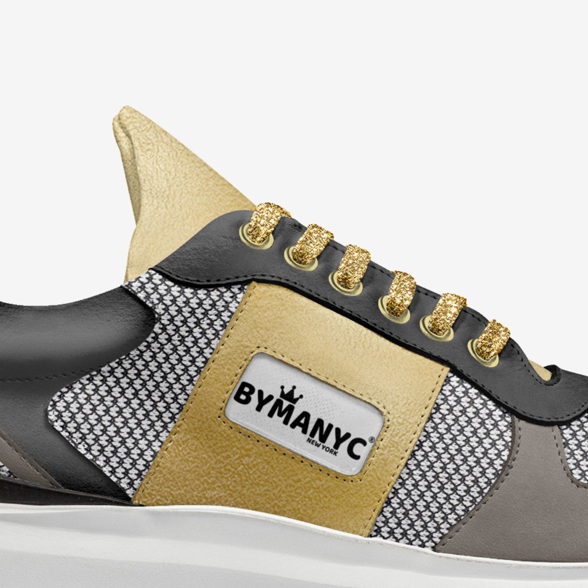 Close-up of a sneaker with gold accents and ByManyc branding on a white background