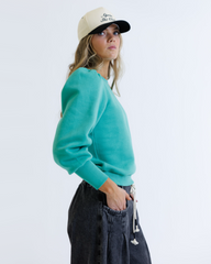 Person wearing a teal sweater and black cap on a white background