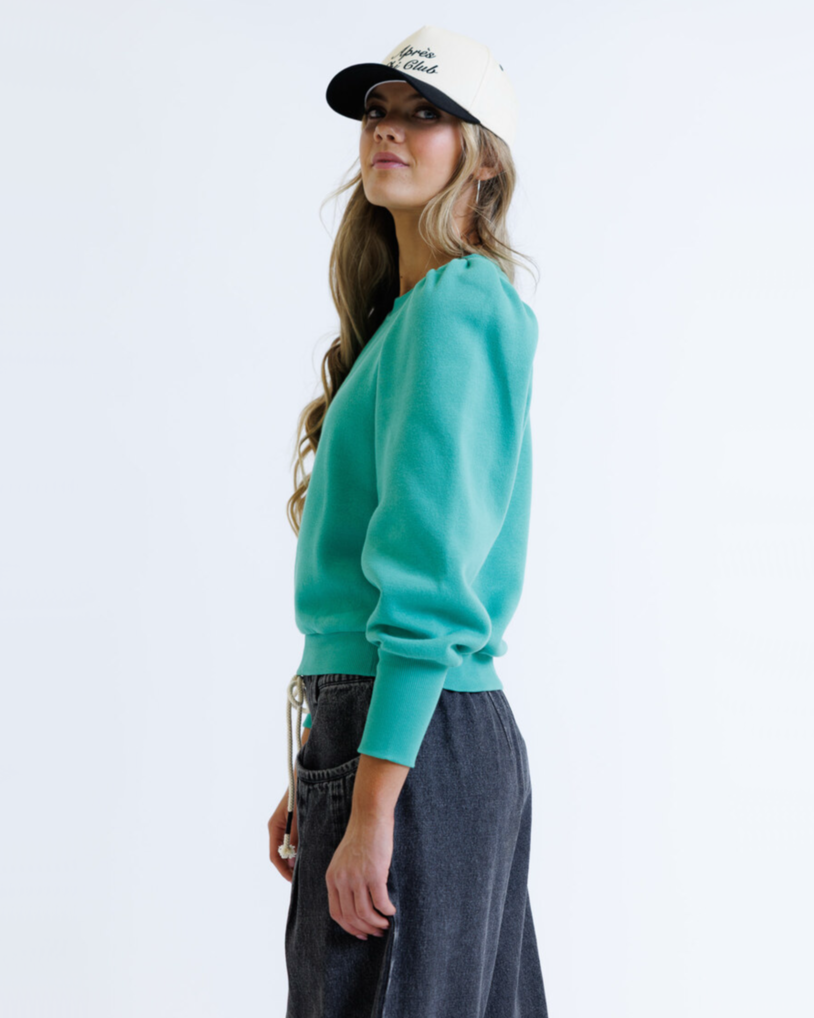 Woman wearing a teal sweater and dark pants on a white background