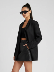 Woman wearing a black pinstripe blazer and leather skirt on a light gray background