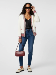 Woman wearing a striped cardigan, black top, blue jeans, and carrying a red handbag on a white background