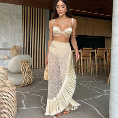 Woman wearing a beige bikini and matching fringe skirt in an outdoor setting.