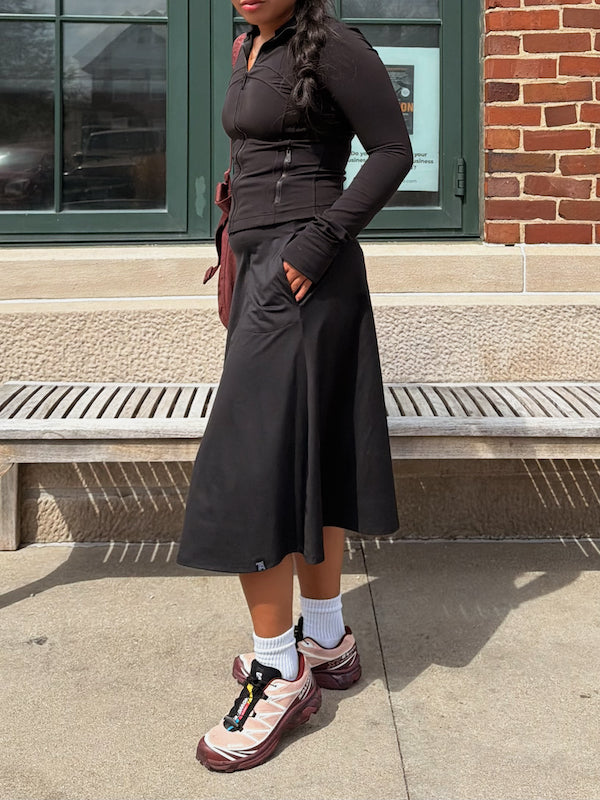 Person wearing a black outfit with pink shoes standing on a sidewalk.