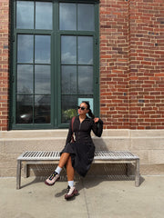 Woman sitting on a bench against a brick wall with large windows.