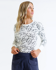Woman wearing a white long-sleeve top with black speckles and navy pants on a white background