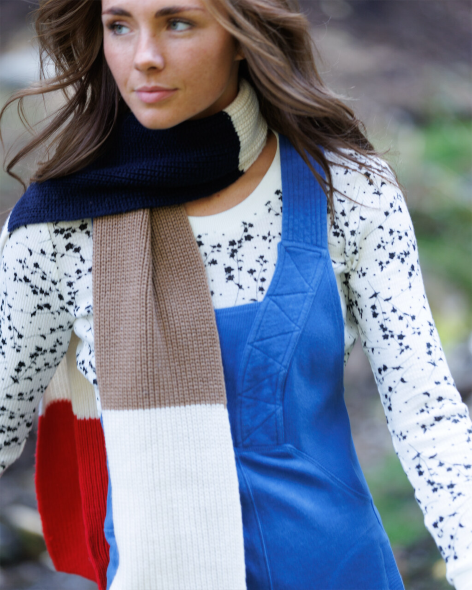 Woman wearing a colorful scarf and blue overalls with a blurred natural background