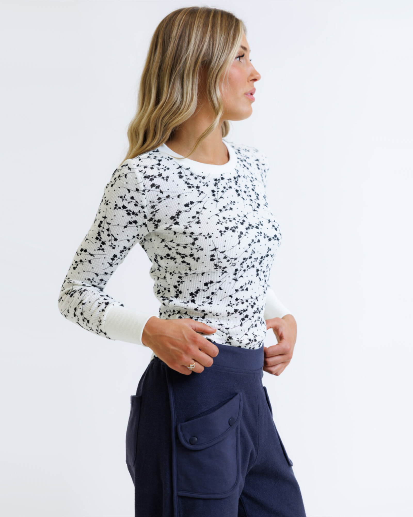 Woman wearing a white long-sleeve top with black speckles and navy pants on a light gray background