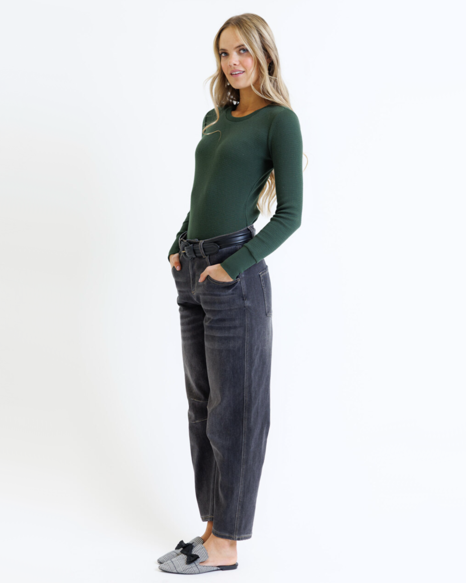 Woman wearing a green sweater and dark jeans on a white background