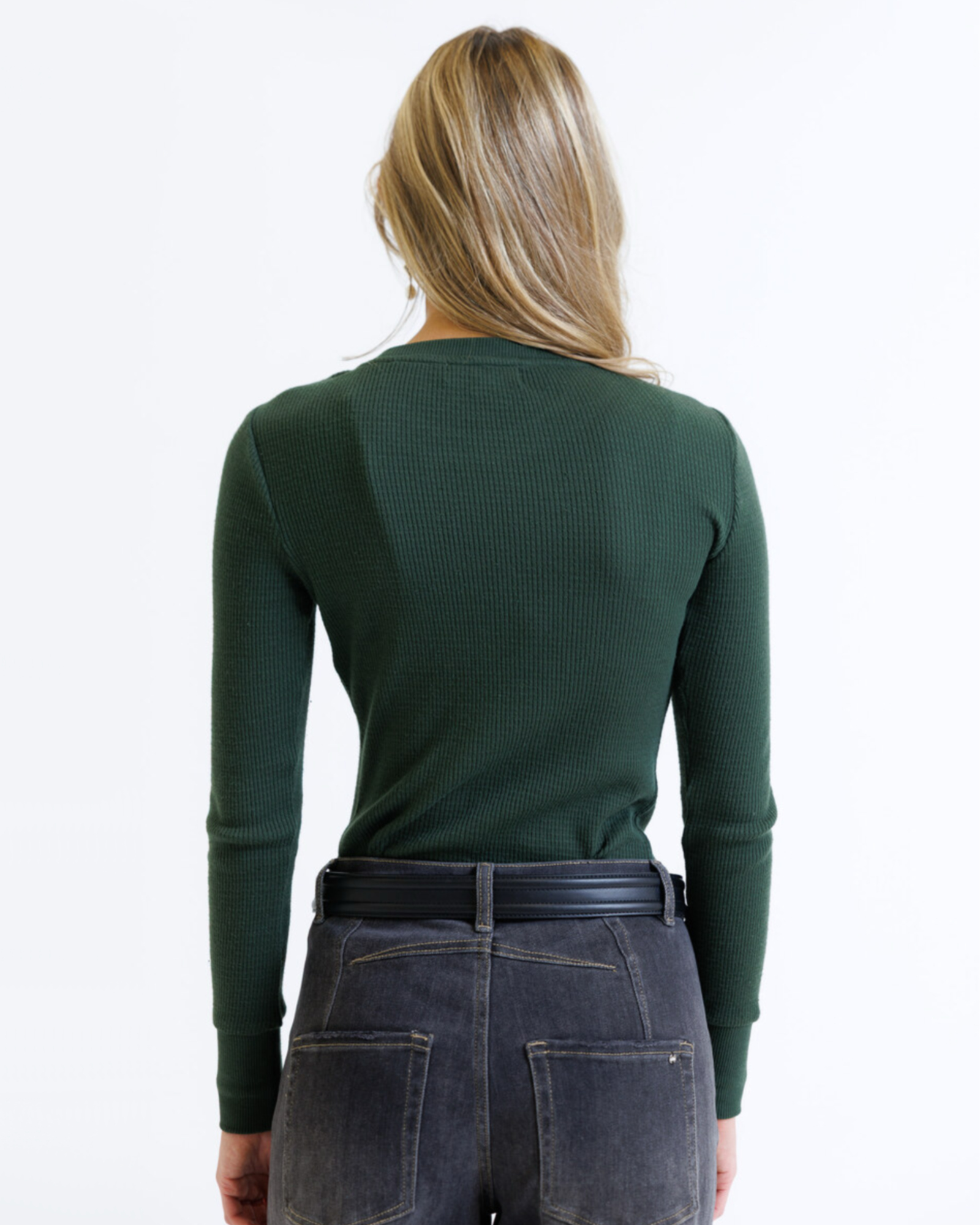 Person wearing a green long-sleeve top and dark jeans on a white background