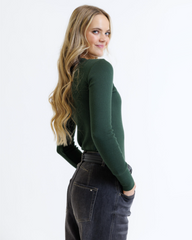 Woman wearing a green sweater and dark jeans on a white background