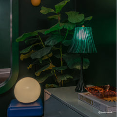 Two lamps, one round and one with a green fiber optic effect, on a surface with a plant in the background.